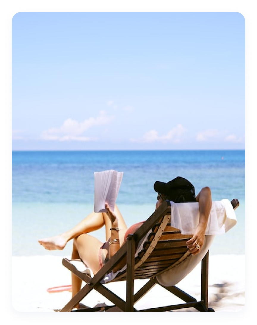 Escena de verano con una persona sentada en una silla de playa de madera, frente al mar, leyendo un libro.